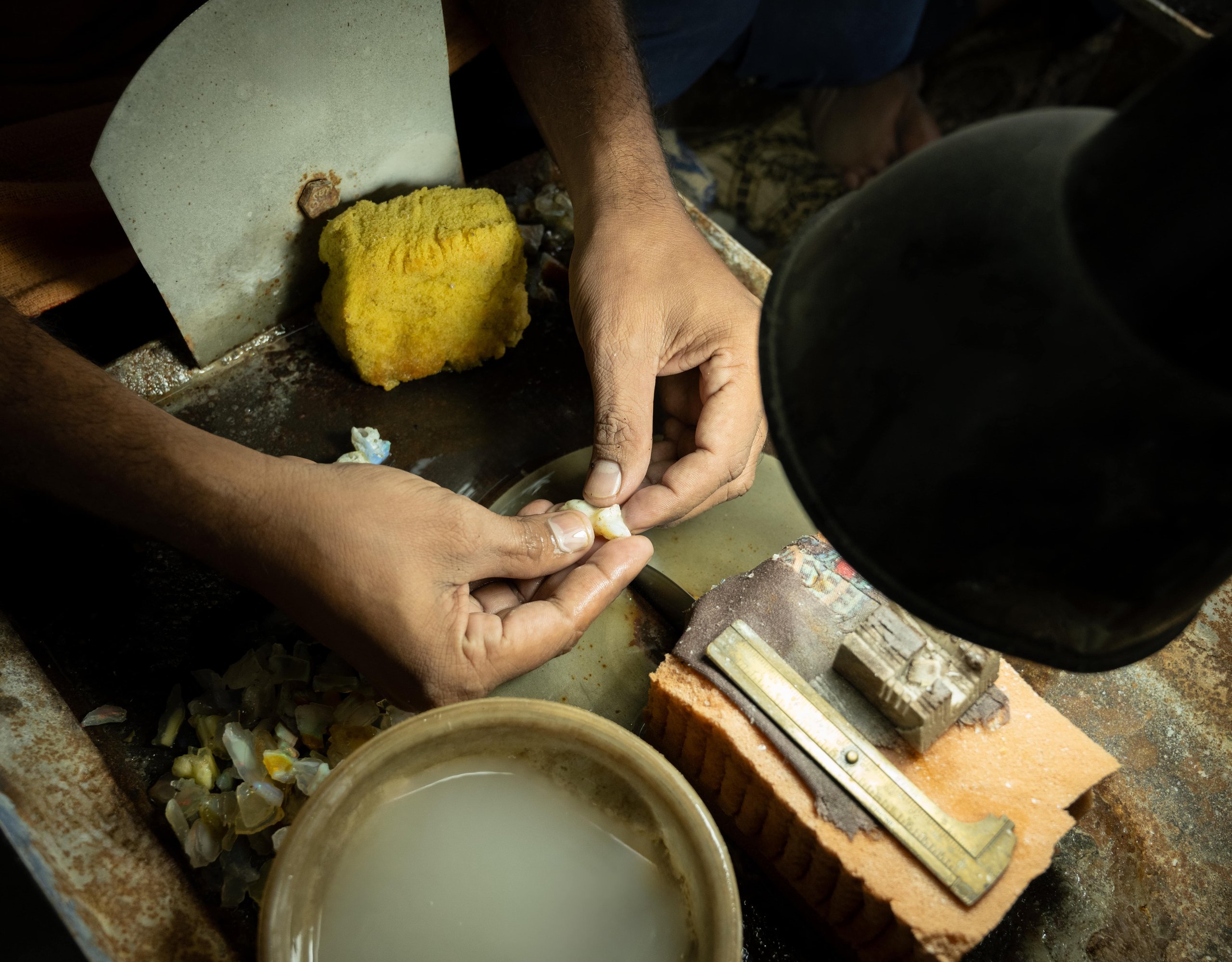 A lapidary artisan shaping a rough opal at the cutting wheel in the Blazels facility